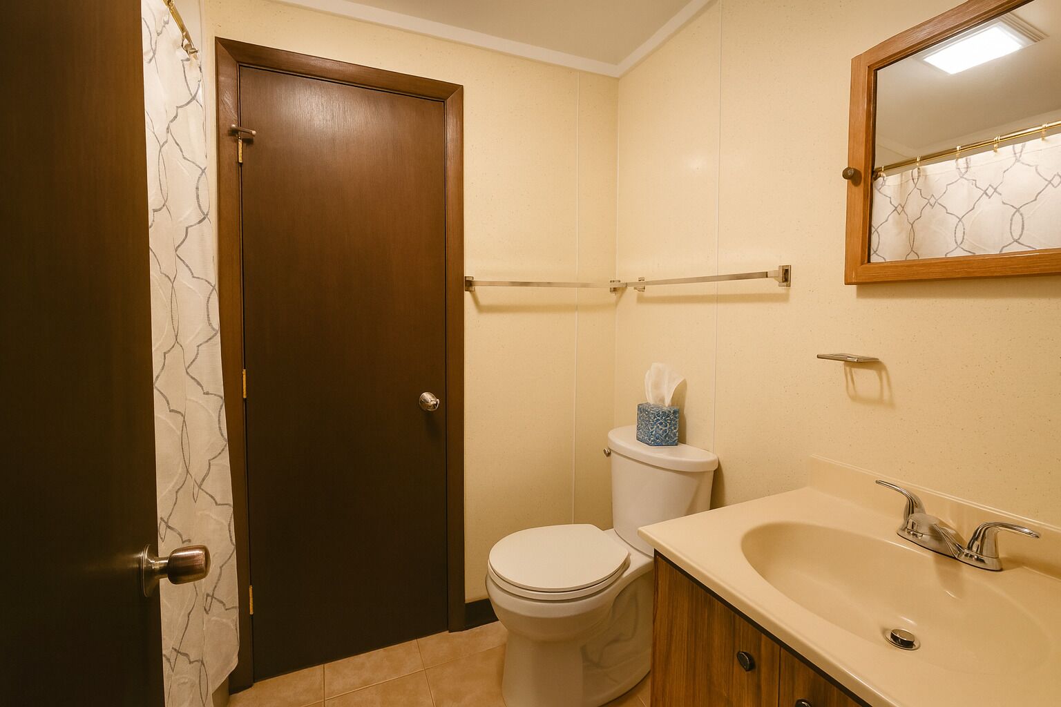Een badkamer met een houten deur, een toilet, een wastafel en een spiegel.