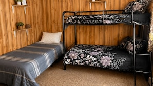 A bunk bed room with two beds, wooden panel walls, and shelves with plants.