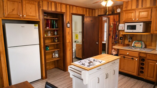 A compact kitchen with wooden cabinets, a refrigerator, a microwave, and a sink.