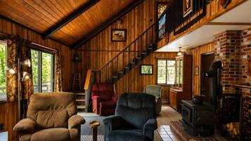 A cozy cabin interior with a wooden staircase, a fireplace, and comfortable seating.