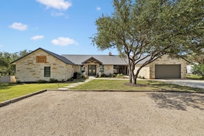 A two-story stone building with a gravel driveway and a tree in the front yard.