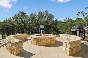 A stone fire pit with a grill and a barbecue in a park setting. - Hidden Creek - near Frio River - 6 bedroom - hot tub - pool - outdoor kitchen (Concan)