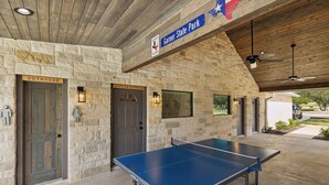 A ping pong table in a covered area with stone walls and doors labeled 'Outhouse' and 'Joplin Express'. - Hidden Creek - near Frio River - 6 bedroom - hot tub - pool - outdoor kitchen (Concan)