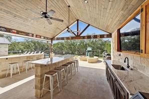 An outdoor bar area with a stone countertop, bar stools, and a grill.