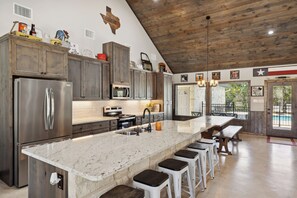 A spacious kitchen with a large island, stainless steel appliances, and a rustic wooden ceiling.