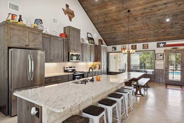 A spacious kitchen with a large island, stainless steel appliances, and a rustic wooden ceiling.