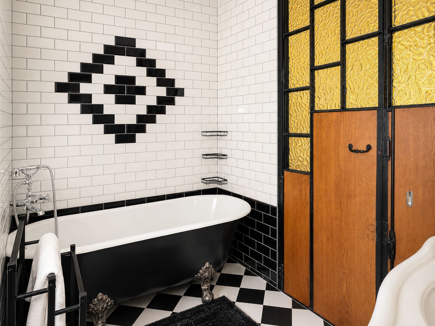 Un bagno con una vasca da bagno nera, pavimento bianco e nero a scacchi, un lavandino bianco e una porta in legno con pannello dorato decorato.