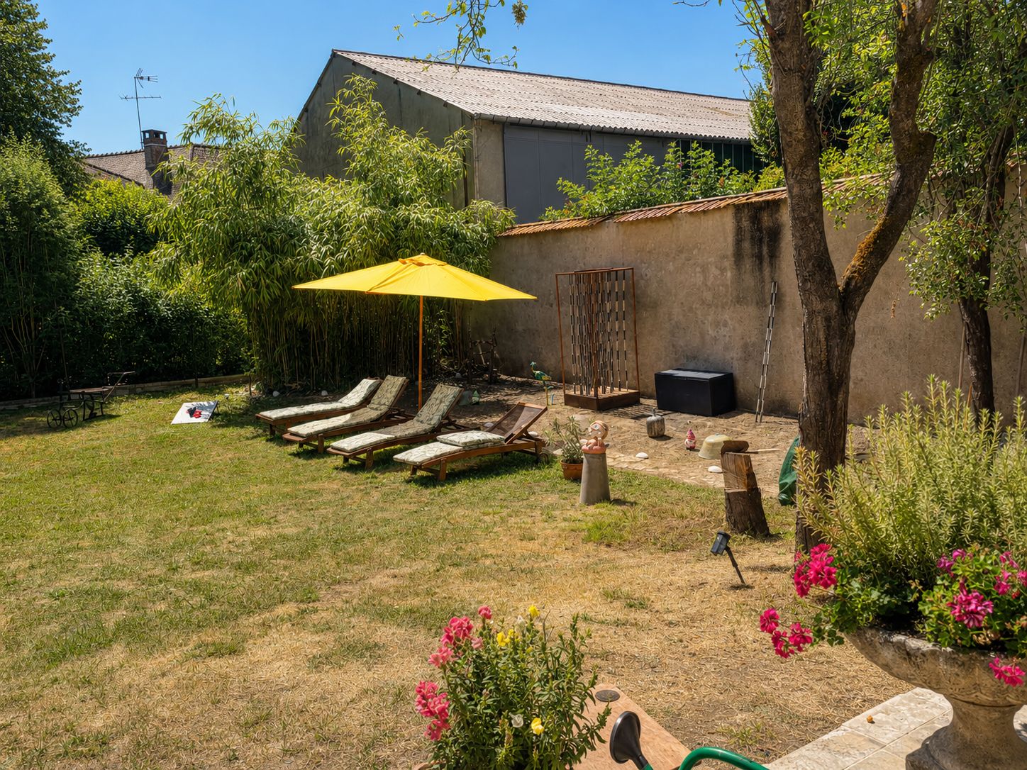 Une cour arrière avec une pelouse, un parasol jaune, des chaises longues et une maison en arrière-plan.