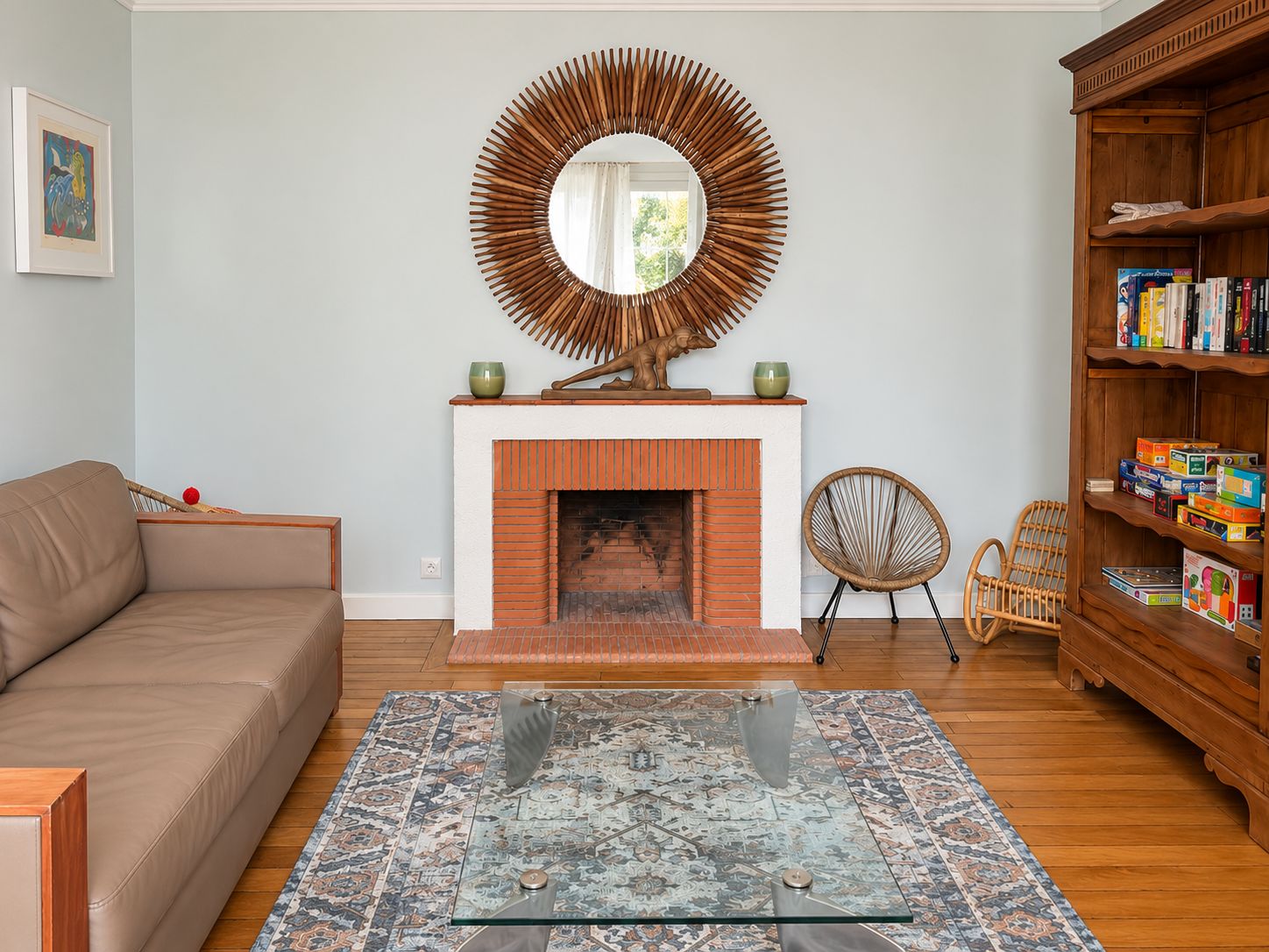 Una sala de estar con chimenea, un sofá, una mesa de centro de vidrio, un sillón de mimbre y una estantería.