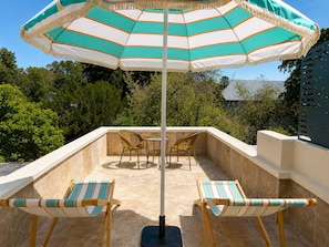Eine Terrasse mit zwei gestreiften Liegestühlen, einem Tisch und einem gestreiften Sonnenschirm.