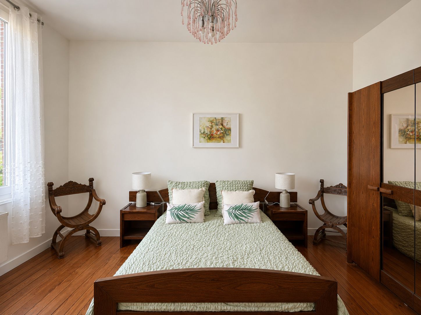 A bedroom with a bed, two nightstands, a chandelier, a window with curtains, and a painting on the wall.