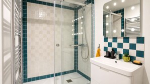 Un bagno moderno con doccia vetro, lavandino bianco e schienale piastrellato.