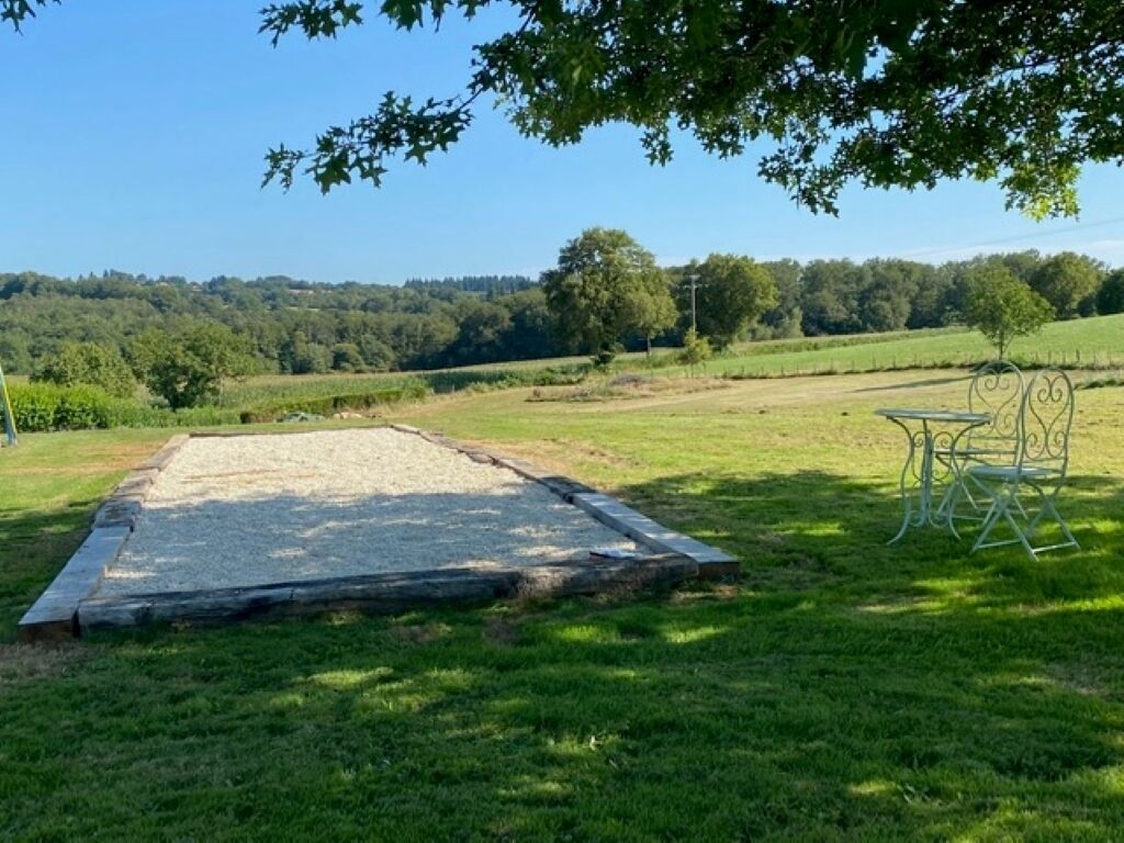 Ein grasbewachsenes Areal mit einem Metalltisch und Stühlen, umgeben von Bäumen und einem klaren Himmel.