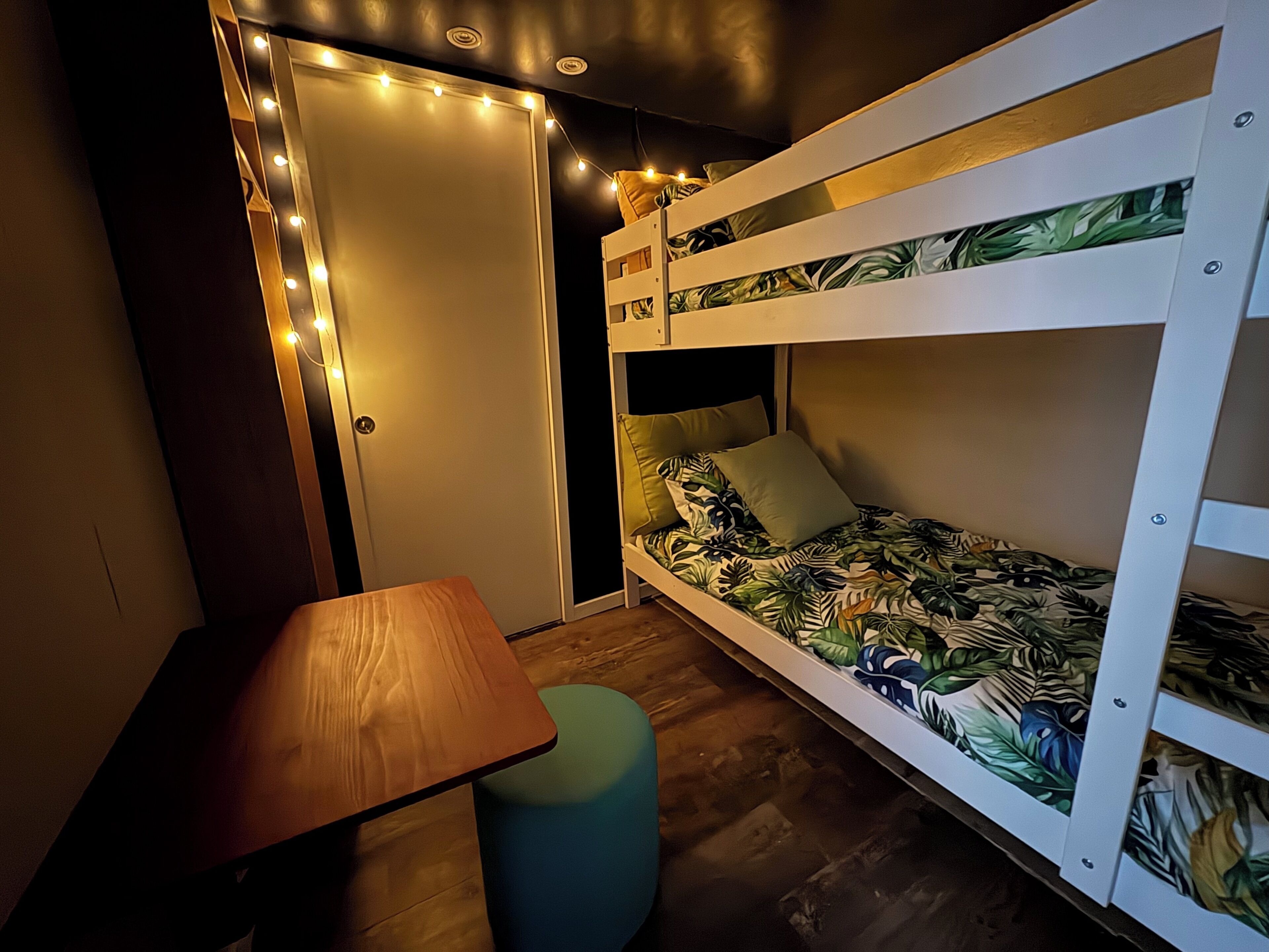 A bunk bed with a tropical-themed bedspread, a small table, and a bench.