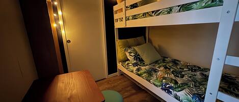Un lit superposé avec une couvre-lit aux motifs tropicaux, une petite table et un banc.