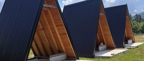 Una hilera de construcciones modernas con techos triangulares, interiores de madera y bases de hormigón, ubicada en un campo cubierto de hierba.