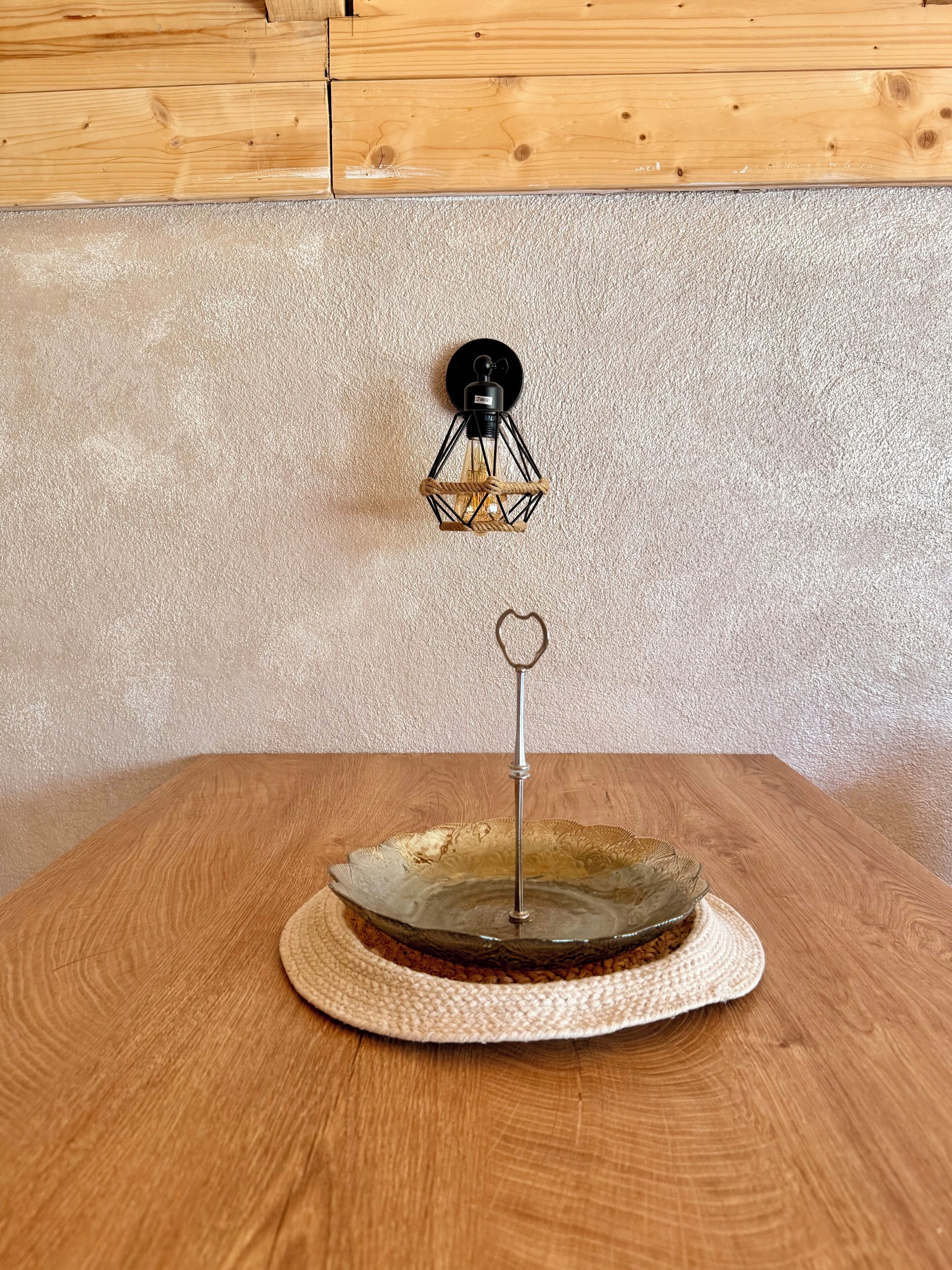 Taula rodona de fusta amb un bol de vidre decoratiu i un suport metàl·lic amb un ornament en forma de cor.