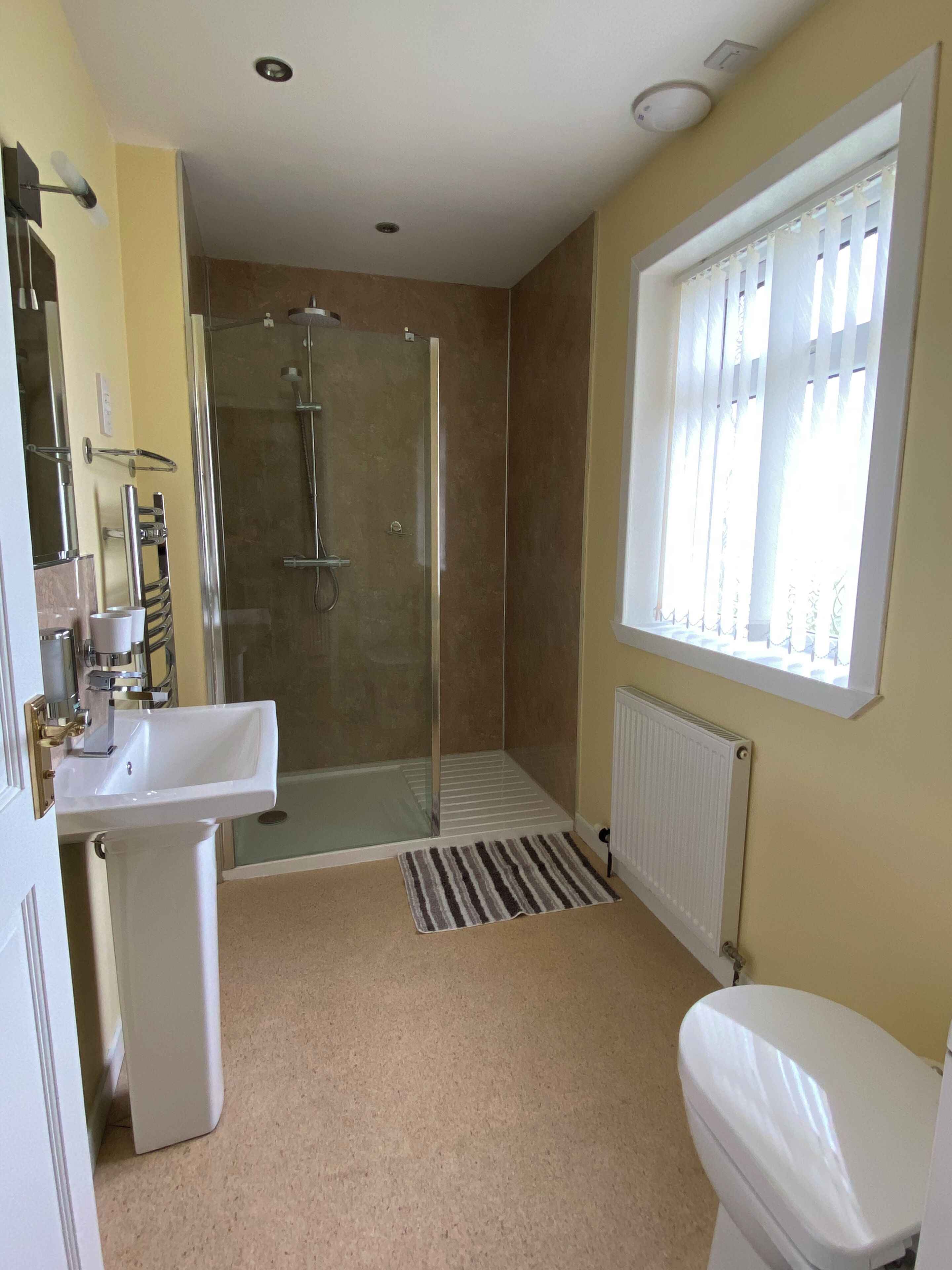 A bathroom with a shower, sink, toilet, and a window with blinds.