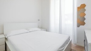 A minimalist bedroom with a large bed, white bedding, a nightstand, and a wall-mounted hexagonal light fixture. - San Gervasio Apartment by Wonderful Italy (Bologna)