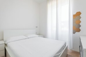 Ein schlicht eingerichtetes Schlafzimmer mit einem großen Bett, weißer Bettwäsche, einem Nachttisch und einer sechseckigen Wandleuchte.