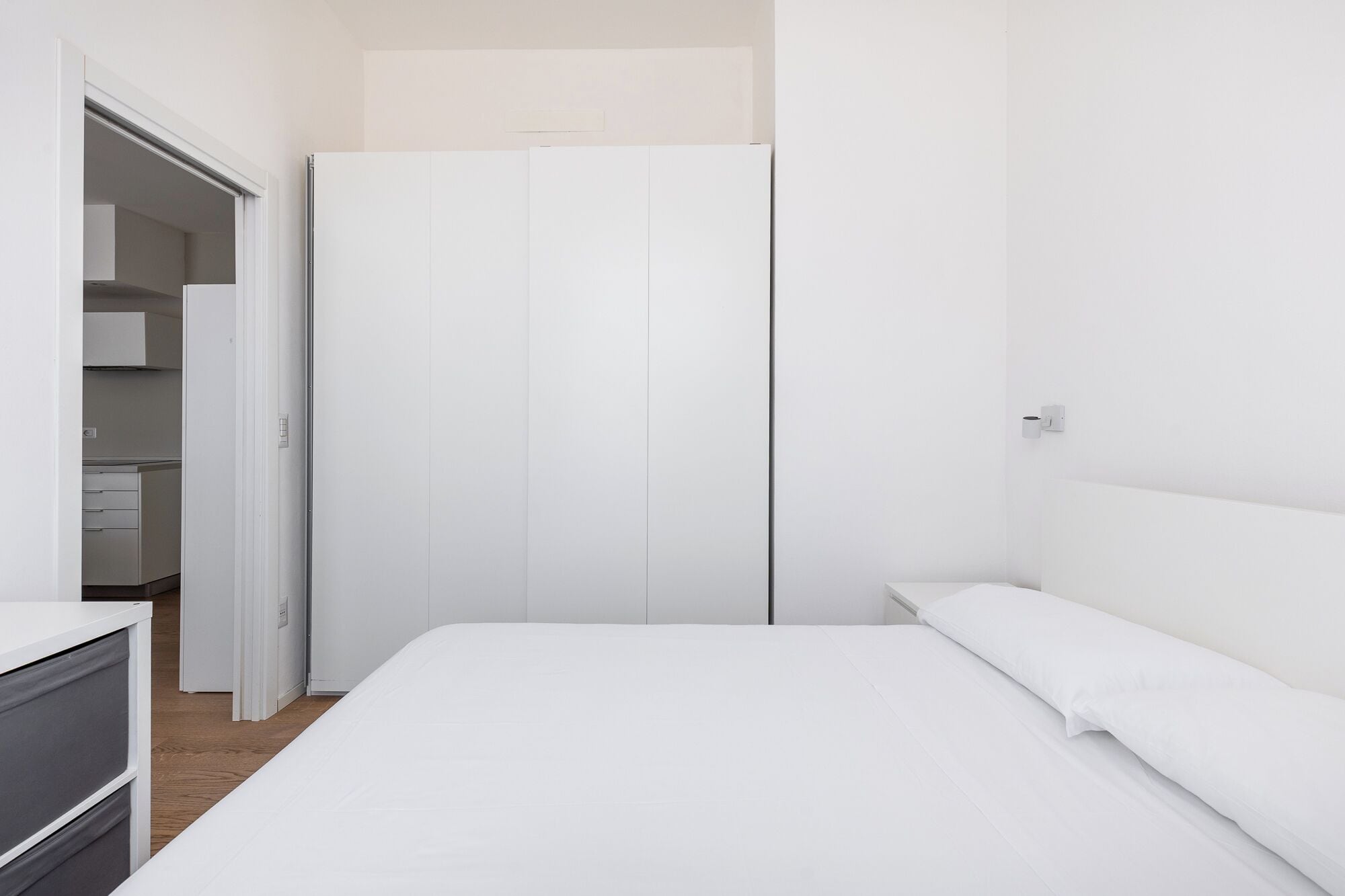 A bedroom with a bed, a wardrobe, and a small kitchenette area.