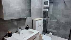 Un baño moderno con un espejo grande, un lavamanos blanco y una zona de ducha.