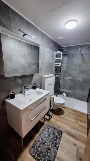 Un baño moderno con un espejo grande, un lavamanos blanco y una zona de ducha.