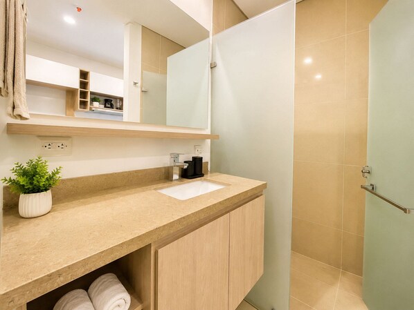 Un baño moderno con encimera color beige, un lavamanos, un espejo, una ducha y una planta en maceta.
