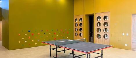 A ping pong table in a room with a climbing wall and a ceiling fan.