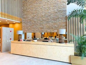 A reception desk with a stone wall backdrop, a wooden door, and a potted plant. - Reserva del Mar II Apartment - Cantamar SOHO -391A (Santa Marta)