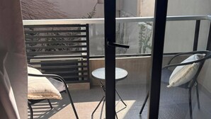 A balcony with a glass door, a round table, two chairs, and a metal railing.