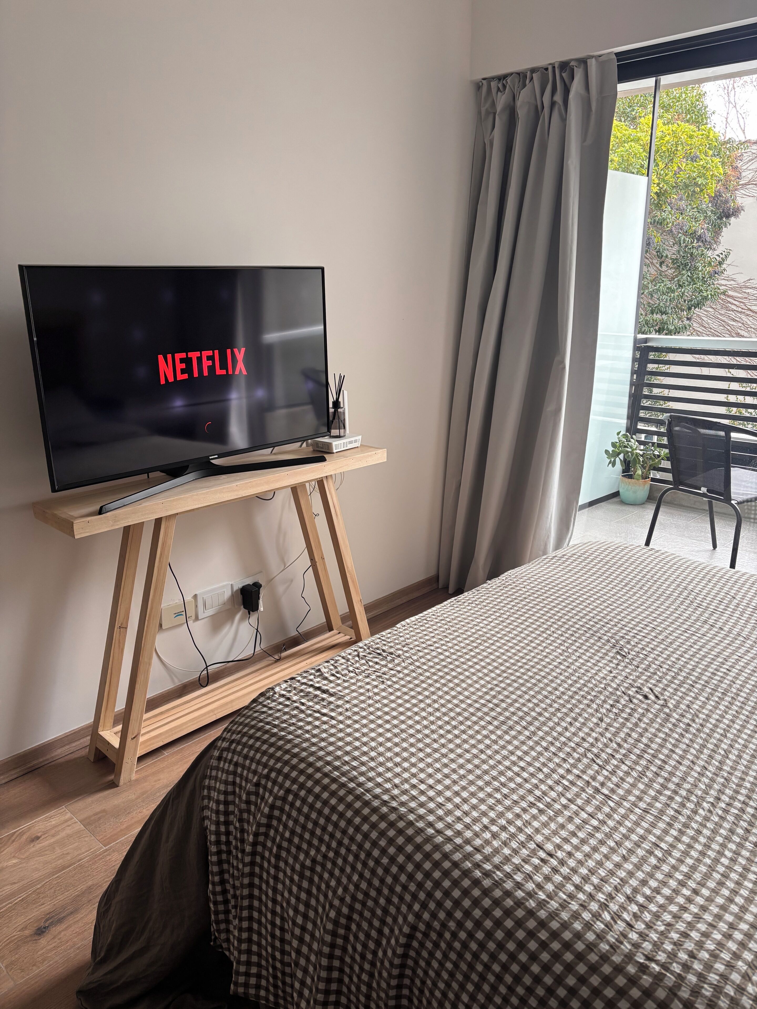 Een kamer met een bed, een televisie op een houten dressoir, een potplant en uitzicht op het omliggende landschap.