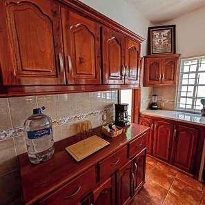 A kitchen with wooden cabinets, a large water dispenser, a coffee maker, and a window with a view. - Casa Sol Bacocho (Puerto Escondido)
