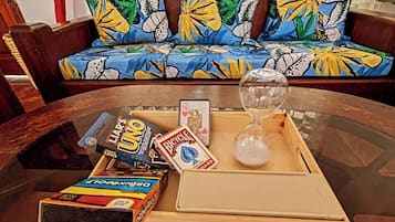A glass coffee table with board games, a dice, and an hourglass on a wooden tray.