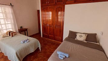 A room with two beds, a ceiling fan, wooden wardrobes, and a tiled floor.