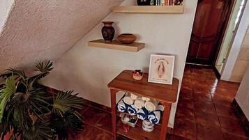 A corner with a shelf holding books and a small vase, a wooden table with towels, and a potted plant.