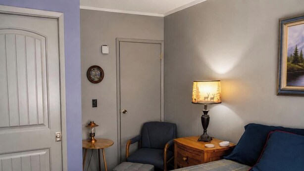 A hotel room with a bed, a chair, a small table with a lamp, a bedside table with a lamp, and a painting on the wall. - Big Bear Escape: Cozy Fireplace! Dine Al Fresco! (Big Bear City)