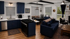 A modern kitchen with dark blue cabinets, a central island with a stove, and a dining area with a dark blue sofa. - Big Bear Escape: Cozy Fireplace! Dine Al Fresco! (Big Bear City)