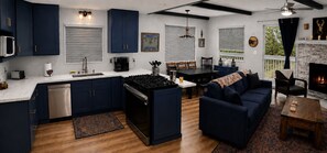 A modern kitchen with dark blue cabinets, a central island with a stove, and a dining area with a dark blue sofa. - Big Bear Escape: Cozy Fireplace! Dine Al Fresco! (Big Bear City)