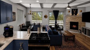 A modern kitchen with a central island, a dining area with a sofa, and a living room with a fireplace. - Big Bear Escape: Cozy Fireplace! Dine Al Fresco! (Big Bear City)