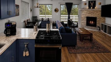 Una cocina moderna con una isla central, un comedor con sofá y una sala de estar con chimenea.