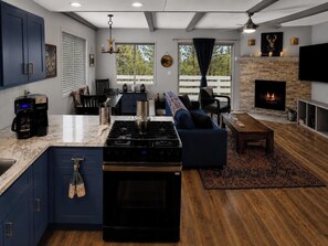 A modern kitchen with a central island, a dining area with a sofa, and a living room with a fireplace. - Big Bear Escape: Cozy Fireplace! Dine Al Fresco! (Big Bear City)