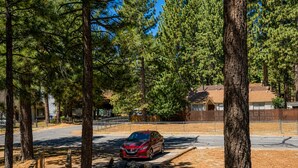 A parking area with a red car, surrounded by trees and a fence. - Big Bear Escape: Cozy Fireplace! Dine Al Fresco! (Big Bear City)