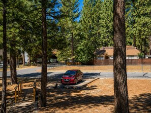 A parking area with a red car, surrounded by trees and a fence. - Big Bear Escape: Cozy Fireplace! Dine Al Fresco! (Big Bear City)