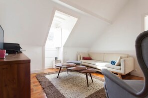 Ein stilvoller Loft-Wohnraum mit schrägem Dach, einer Couch, einem Couchtisch und einem Sessel.