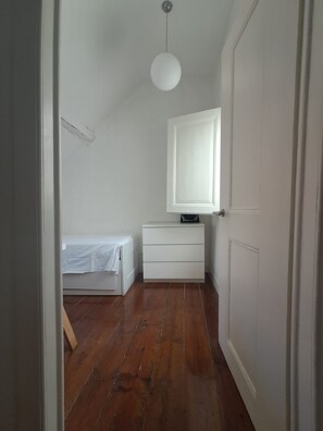 Ein schmaler Flur mit einem Bett, einer Kommode und einer Tür.