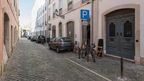 Een straat met keien, omzoomd door gebouwen, met een geparkeerde auto en een fiets.