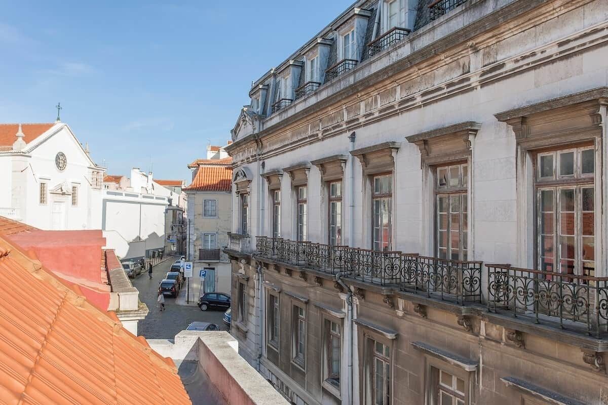 A building with classical architecture, featuring a balcony with wrought iron railings and a street view below.