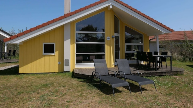 Ein gelbes Gebäude mit rotem Dach, großen Fenstern und einer Terrasse mit Außenbestuhlung.