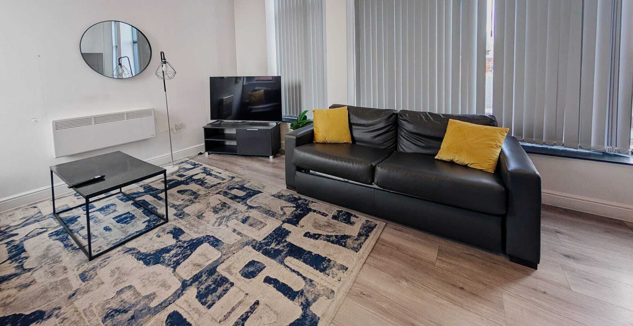 A modern living room with a black leather sofa, a small black table, a large mirror, and a TV.
